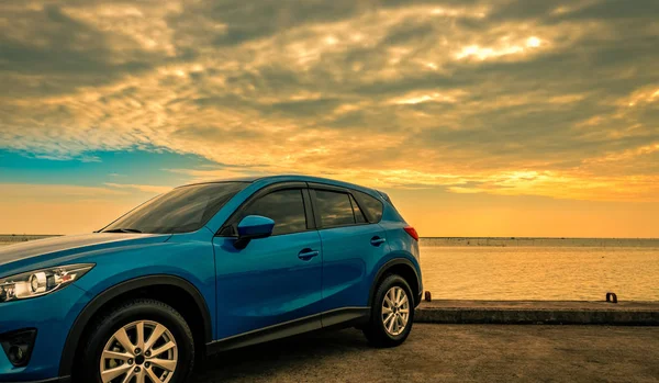 Carro SUV compacto azul com esporte e design moderno estacionado na estrada de concreto por mar ao nascer do sol. Tecnologia amiga do ambiente. Tecnologia de carro híbrido e elétrico. Lugar de estacionamento. viagens de verão . — Fotografia de Stock