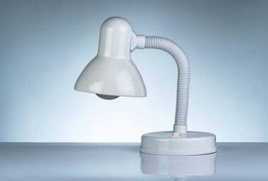 White modern table lamp isolated on white table on gradient background. Desk lamp for reading a book in dormitory room. Home and office furniture with minimalist design. Desk spotlight.