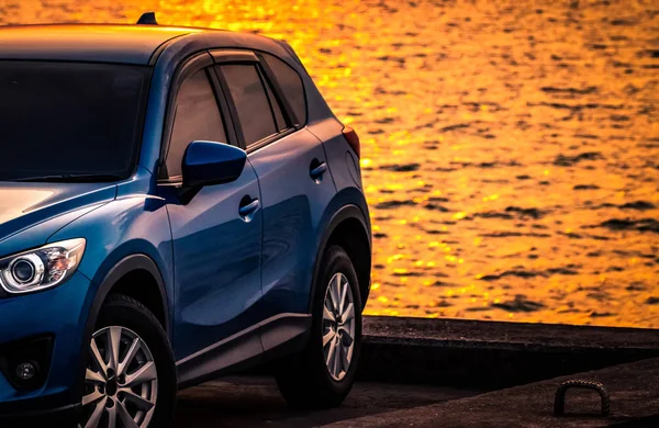 Carro SUV compacto azul com esporte e design moderno estacionado na estrada de concreto por mar ao pôr do sol. Tecnologia amiga do ambiente. Tecnologia de carro híbrido e elétrico. Lugar de estacionamento. viagens de verão . — Fotografia de Stock