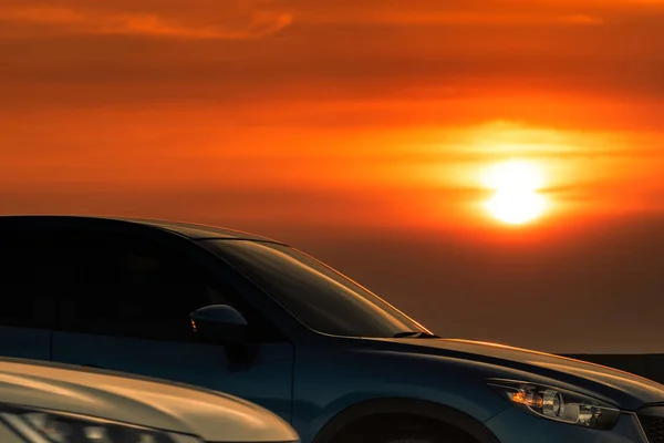 Πλευρική θέα του μπλε SUV με αθλητισμό και μοντέρνο σχεδιασμό σταθμευμένο σε τσιμεντένιο δρόμο κατά το ηλιοβασίλεμα. Υβριδική και ηλεκτρική τεχνολογία αυτοκινήτων. Ταξιδάκι. Αυτοκινητοβιομηχανία. Χώρος στάθμευσης αυτοκινήτων με όμορφο ηλιοβασίλεμα. — Φωτογραφία Αρχείου