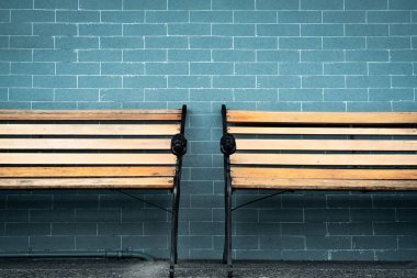 Yeşil tuğla duvar arka plan üzerinde boş iki ahşap tezgah. Birinin boş tahta sandalyeyi doldurmasını bekliyorum. Binanın dışında kahverengi ahşap bank. Bekleme konsepti. Teklif için yer olan boş duvar.