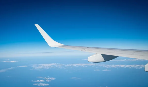 Wing of plane over white clouds. Airplane flying on blue sky. Scenic view from airplane window. Commercial airline flight. Plane wing above clouds. Flight mechanics concept. International flight.