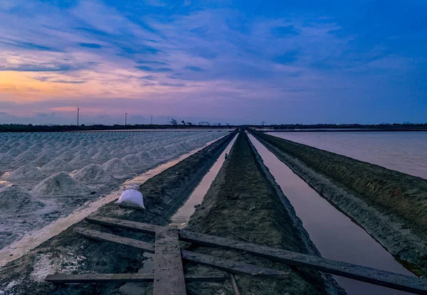 Granja de sal por la mañana con cielo y nubes al amanecer. Paisaje de campo de sal marina en Tailandia. Agua de mar en el canal y camino del suelo en la granja. Materia prima de sal industrial. Turismo de verano en Tailandia . — Foto de Stock