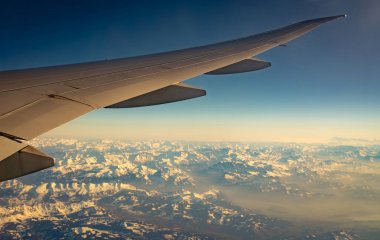 Beyaz kar ile dağ örtüsü üzerinde düzlem kanat. Mavi gökyüzünde uçan uçak. Uçak penceresinden manzara. Ticari havayolu uçuşu. Uçak kanadı. Uçuş mekaniği kavramı. Uluslararası uçuş.