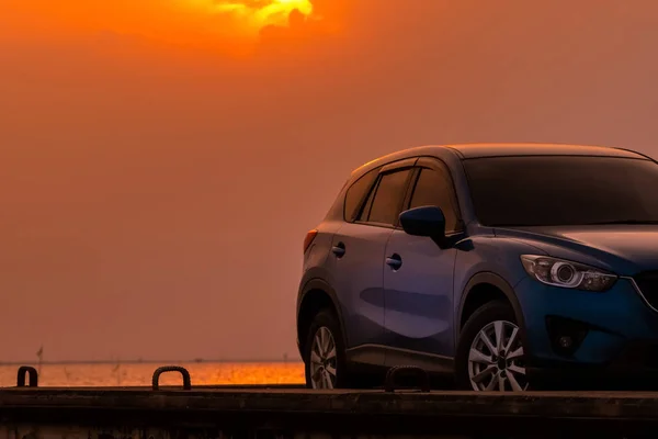 Coche SUV azul compacto con diseño deportivo y moderno estacionado en carretera de hormigón junto al mar al atardecer por la noche. Concepto de tecnología de coche híbrido y eléctrico. Plaza de aparcamiento. Industria automotriz . — Foto de Stock