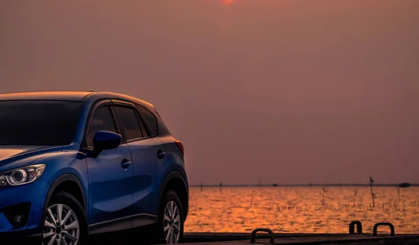 Kék kompakt Suv autó sport és a modern design parkolt a betonút a tenger a naplementét este. Hibrid és elektromos autó technológiák fogalma. Parkolóhely. Autóipar. — Stock Fotó