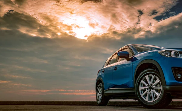 Blauwe compacte Suv auto met sport en modern design geparkeerd op betonnen weg door de zee bij zonsondergang in de avond. Hybride en elektrische auto technologie concept. Parkeerplaats auto. Auto-industrie. — Stockfoto