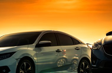 Güzel turuncu ve altın günbatımı gökyüzü ile otoparkta park edilmiş lüks ve modern tasarıma sahip beyaz araba ön görünümü. Otomotiv endüstrisi. Yolculuk yolculuğu. Araba bakımı için parlak beyaz araba arka plan