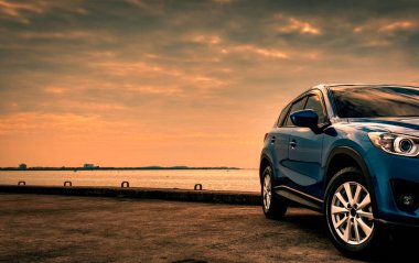 Mavi kompakt Suv araç spor ve modern tasarımı ile akşam günbatımında denizin kenarında beton yolda park etmiş. Hibrit ve elektrikli otomobil teknoloji kavramı. Araba park yeri. Otomotiv Sanayi. 