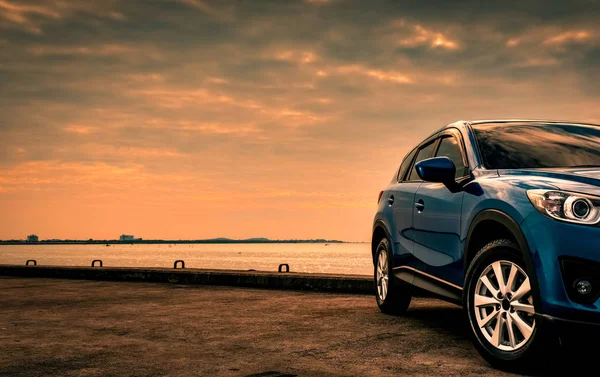 Blauwe compacte Suv auto met sport en modern design geparkeerd op betonnen weg door de zee bij zonsondergang in de avond. Hybride en elektrische auto technologie concept. Parkeerplaats auto. Auto-industrie. — Stockfoto