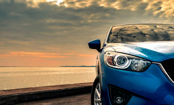 Coche SUV azul compacto con diseño deportivo y moderno estacionado en carretera de hormigón junto al mar al atardecer por la noche. Concepto de tecnología de coche híbrido y eléctrico. Plaza de aparcamiento. Industria automotriz . — Foto de Stock