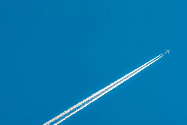 Airplane with white condensation tracks. Jet plane on clear blue sky with vapor trail. Travel by aeroplane concept. Trails of exhaust gas from airplane engine. Aircraft with white stripes. — Stock Photo, Image