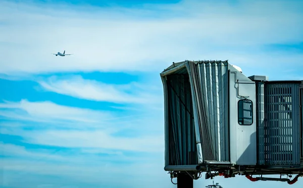 Jet bridge dopo la linea aerea commerciale decolla in aeroporto e l'aereo vola nel cielo blu e nuvole bianche. Ponte di imbarco passeggeri degli aerei attraccato. Volo di partenza della compagnia aerea internazionale . — Foto Stock