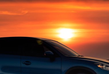 Gün batımında deniz plajı ile beton yolda park edilmiş spor ve modern tasarıma sahip mavi Suv araba yan görünümü. Elektrikli araba teknolojisi. Yolculuk yolculuğu. Otomotiv endüstrisi. Kırmızı ve sarı gün batımı gökyüzü.