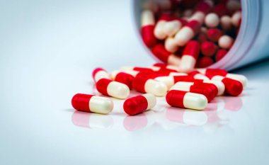 Uyuşturucu şişesinin bulanık arka planında beyaz masada kırmızı-beyaz kapsül hapları. Antibiyotikler ilaç direnci. Antimikrobiyal kapsül hapları. İlaç endüstrisi. Eczane. Küresel sağlık kavramı. 
