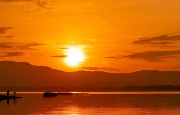 Vacker soluppgång himmel ovanför berget vid reservoaren. Folk fiskar med ett fiskespö på älven. Landskap av reservoar och berg med orange soluppgång himmel. Siluett liv på morgonen. — Stockfoto