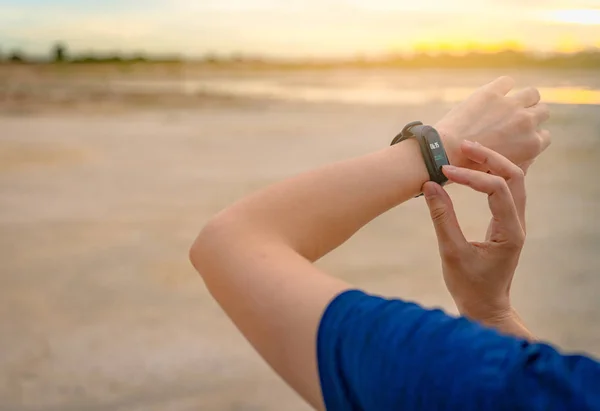 Mujer asiática joven tocando banda inteligente después de correr en la mañana. Computadora portátil. Pulsera monitor de frecuencia cardíaca. Aparato Fitness. Rastreador de actividad o fitness. Reloj inteligente dispositivo conectado. Muñequera — Foto de Stock