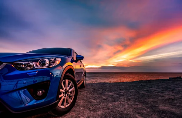 Kék kompakt SUV autó a sport és a modern design parkolt a tengerparton naplementekor. Hibrid-és elektromos autó-technológia. Parkolóhelyet. Autóipar. Autóápolási üzleti háttér. Gyönyörű ég. — Stock Fotó