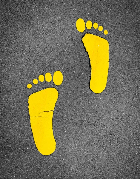 Yellow footprint painted on asphalt road. Walkway lane traffic sign. Foot mark on street texture background. Direction sign. Yellow footstep on tarmac floor. One step towards a better future concept. — Stock Photo, Image