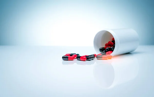 Red-black antibiotic capsule pills spread out of plastic drug bottle on white background. Pharmaceutical industry. Antibiotic drug resistance. Pharmaceutical manufacturing. Antimicrobial drug pills.