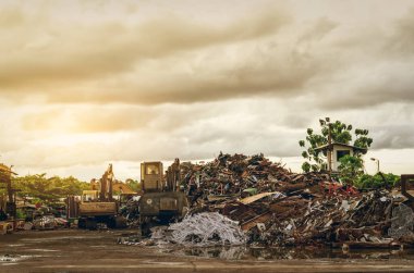 Çöp yığını ve kazan atık deposunda. Çöp geri dönüşüm işi. Ormandaki yeşil ağaçların yanındaki hurdalıkta plastik atıklar, odun kırıntıları ve eski paslı metaller. Geri dönüşüm için plastik çöp.