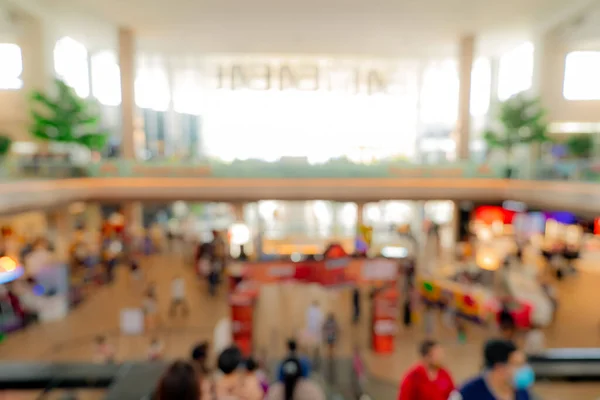 Blur crowded people inside shopping mall. Defocus retail shop in shopping center with bokeh background. People walking and on escalator at first floor of building. Shopping mall interior. Retail store