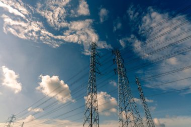 Mavi gökyüzüne ve beyaz bulutlara karşı yüksek voltajlı elektrik pilonu ve elektrik kablosu. Elektrik direğinin güneş ışığıyla alt görüntüsü. Kablo kablolu yüksek voltaj şebekesi kulesi. Güç ve enerji kavramı. 