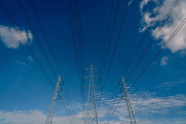 High voltage electric pylon and electrical wire against blue sky and white clouds. Looking up view of Electricity pylon. High voltage grid tower with wire cable.  Power and energy concept.