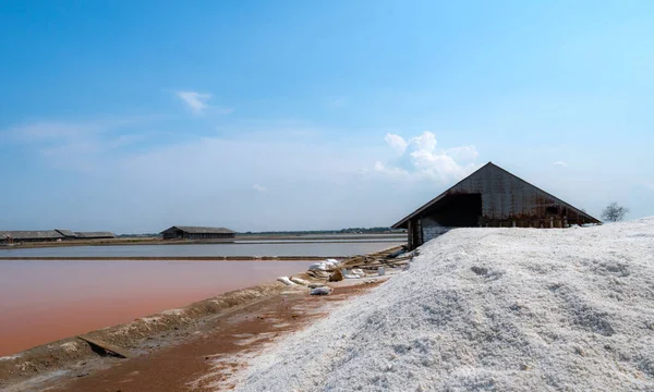 Landscape of brine salt farm with blue sky on sunny day. Salt warehouse. Pile of organic sea salt. Raw material of salt industrial. Sodium chloride mineral. Evaporation of sea water. Iodine.