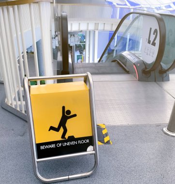 Alışveriş merkezindeki yürüyen merdivenin önündeki sarı panoda eşit olmayan taban uyarı levhasına dikkat edin. Şafak sökmeden önce yürüyen merdivende güvenlik için düz olmayan kat uyarı levhasına dikkat edin. Güvenlik uyarısı.