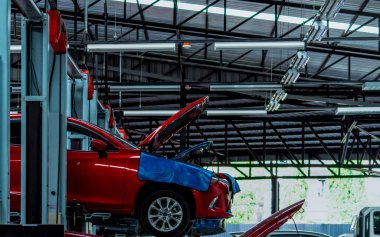 Otomobil tamircisi. Kırmızı SUV arabası tamirat ve bakım için garaja kaldırıldı. Kaldırılmış araçla otomobil servisi. Araba teftiş için atölyeden kaldırıldı. Benzin istasyonunda araç kontrolü..