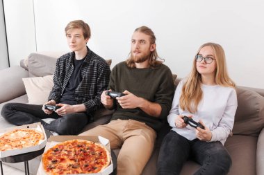 Koltukta oturuyor ve video oyunları birlikte evde oynayan arkadaş grubu. İki erkek ve pizza yemek ve iskambil izole spor kız portresi