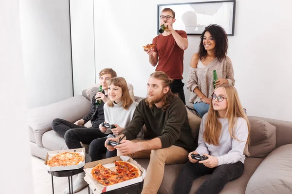 Group of smiling friends spending time together while playing video games,eating pizza and drinking beer at home