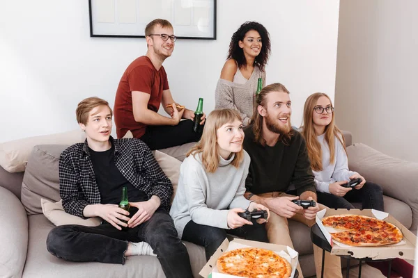 Group of friends sitting on sofa and spending time together while playing video games,eating pizza and drinking beer at home