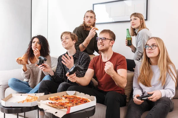Portrait of cool friends sitting on sofa and spending time together while playing video games,eating pizza and drinking beer at home. Group of young people showing different emotions isolated