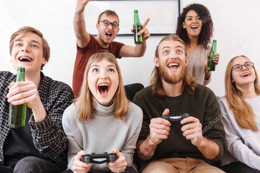 Close up photo of excited friends sitting on sofa and spending time together while playing video games and drinking beer  at home 