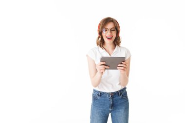 Genç hanımefendi gözlük ve izole beyaz arka plan üzerinde elinde tablet ile ayakta kulaklık portresi