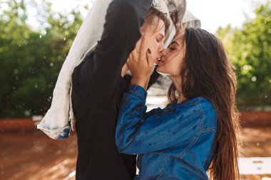 Ayakta ve kendilerini denim ceket ile her diğer yağmur altında öpüşme sırasında kapsayan genç çift portresi. Park tarihte güzel çift