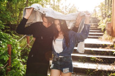 Genç güzel çift kendilerini denim ceket ile birlikte parkta yağmur altında giderken kapsayan portresi