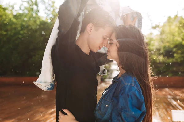 年轻的微笑夫妇的肖像覆盖自己的牛仔夹克 而站在雨中公园 美丽的情侣一起共度时光 — 图库照片