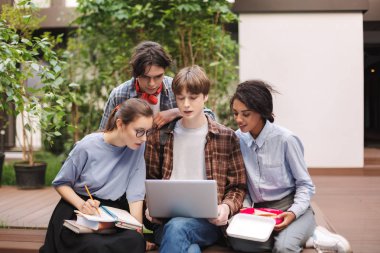 Grup Genç öğrenci kitap ve diz ve birlikte eğitim Üniversitesi avluda laptop ile bankta oturmuş 