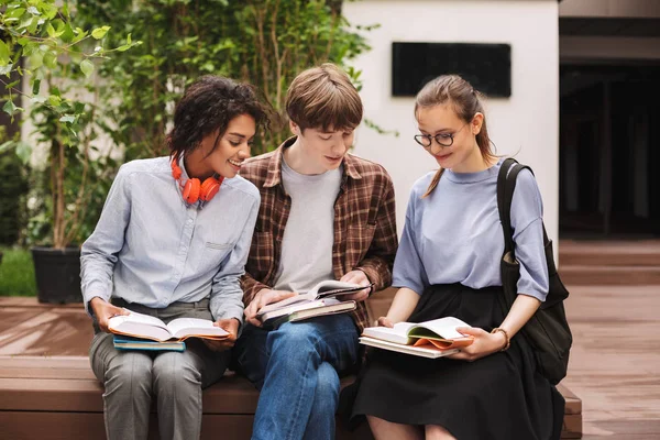 Grupa Studentów Uśmiechający Się Siedząc Ławce Czytanie Książek Dziedzińcu Uniwersytetu — Zdjęcie stockowe