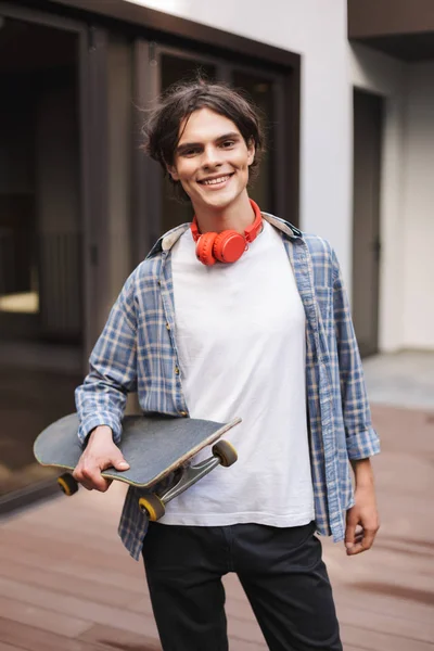 Pemuda Tersenyum Dengan Headphone Merah Berdiri Dan Memegang Skateboard Sambil — Stok Foto