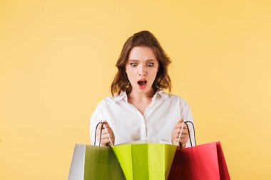 Ayakta ve amazedly renkli alışveriş poşetleri ellerinde renkli arka plan üzerinde seyir genç shoked kadın