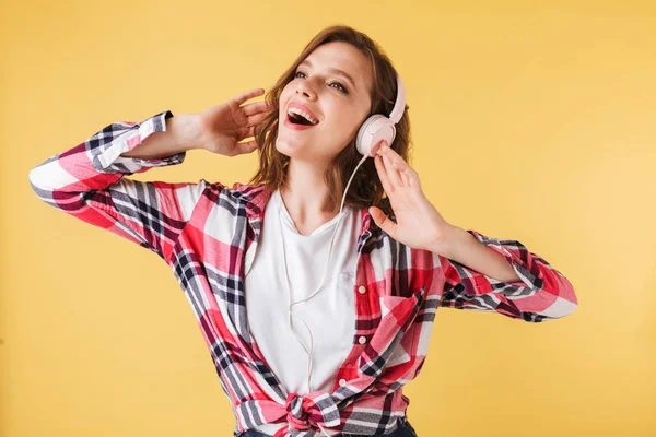 Young pretty lady in colorful shirt standing and singing while listening music in headphones on over colorful background