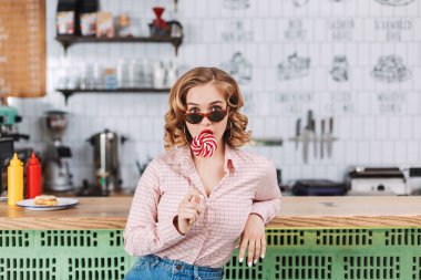 Barda oturan güneş gözlüğü güzel Bayan lolipop şeker ve amazedly kamera arayan kahvede sayaç