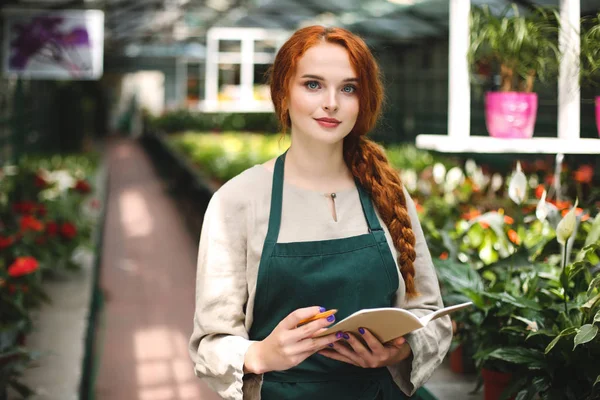 Pretty Smiling Florist Apron Standing Notepad Pencil Hands Dreamily Looking — Stock Photo, Image