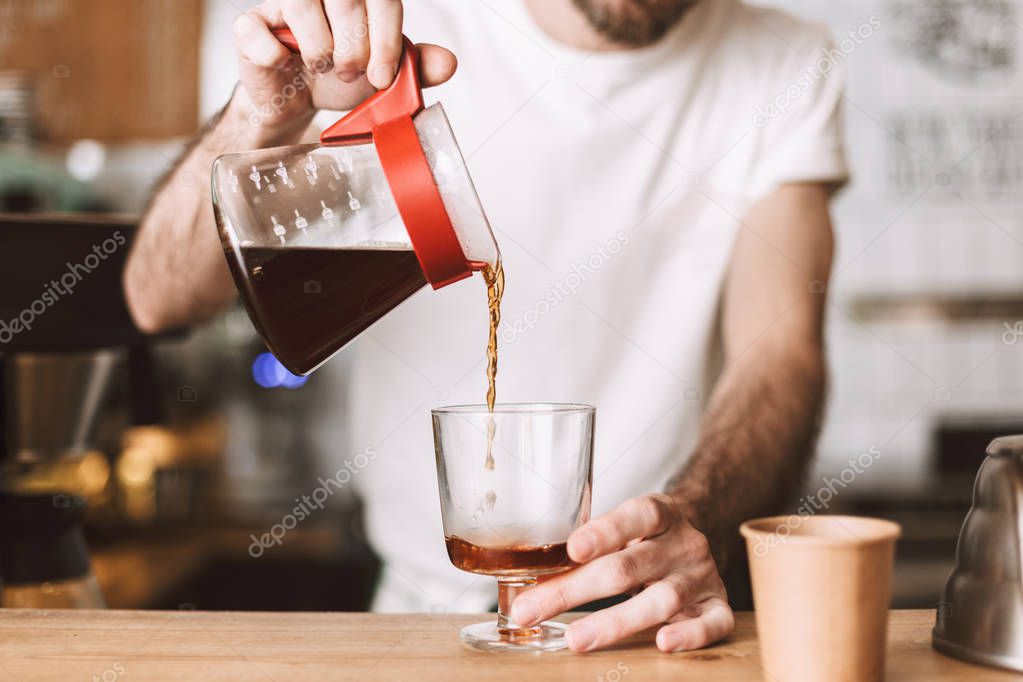 Close up photo of barista at bar counter pouring filter coffee in glass in cafe