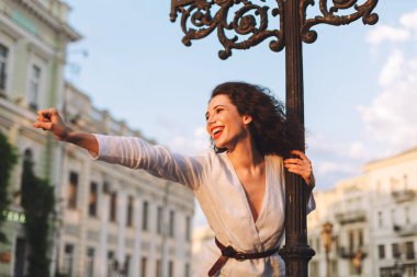 Ayakta ve sevinçle bir yana mutlu bir şekilde sokakta vakit süre seyir Beyaz ceketli genç gülümseyen kadın