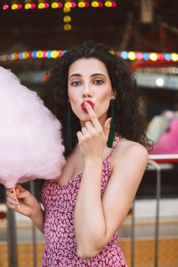 Genç güzel bayan elbise ayakta pembe pamuk şeker kamera seyir eğlence parkında el ve sersem ile siyah kıvırcık saçlı